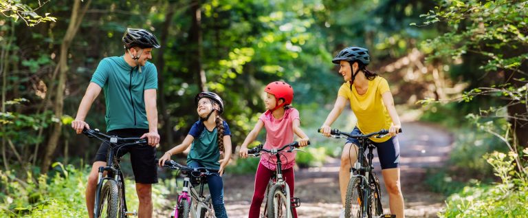 Young family with little children preapring for bike ride, standing with bicycles in nature.